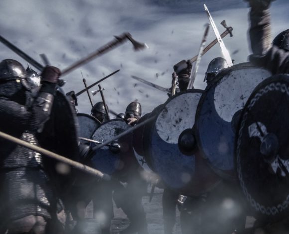 Średniowiecze kojarzy się z bitwami. Na obrazie widoczna rekonstrukcja średniowiecznej bitwy. Rycerze z tarczami i mieczami w zwarciu.