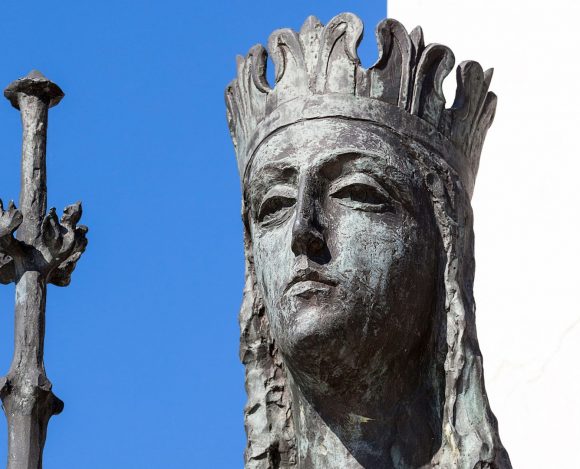 Posąg królowej Jadwigi na tle nieba i ściany białego budynku.