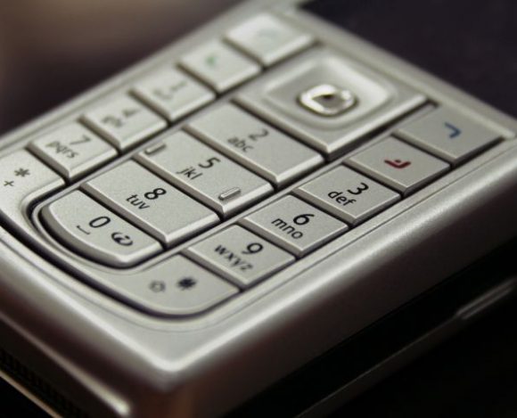 Szary telefon klawiszowy położony na biurku. Jakie są najlepsze ciekawostki o telefonach tego typu i smartfonach?