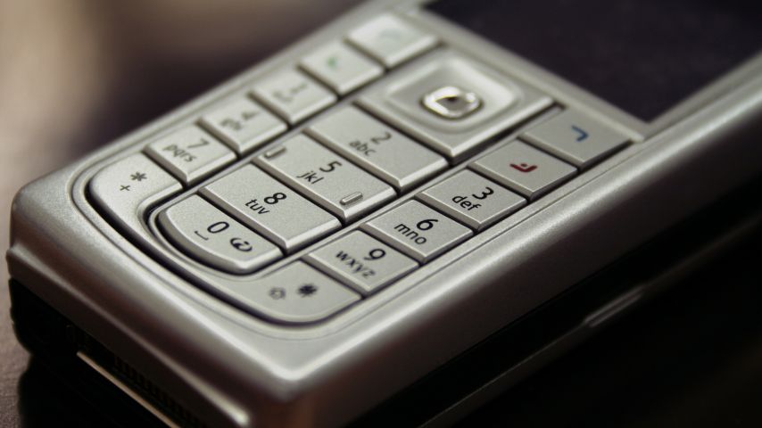 Szary telefon klawiszowy położony na biurku. Jakie są najlepsze ciekawostki o telefonach tego typu i smartfonach?