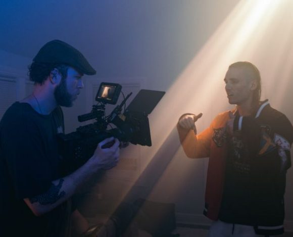 Operator kamery nagrywa teledysk wraz ze śpiewającym piosenkarzem w ciemnym pomieszczeniu.