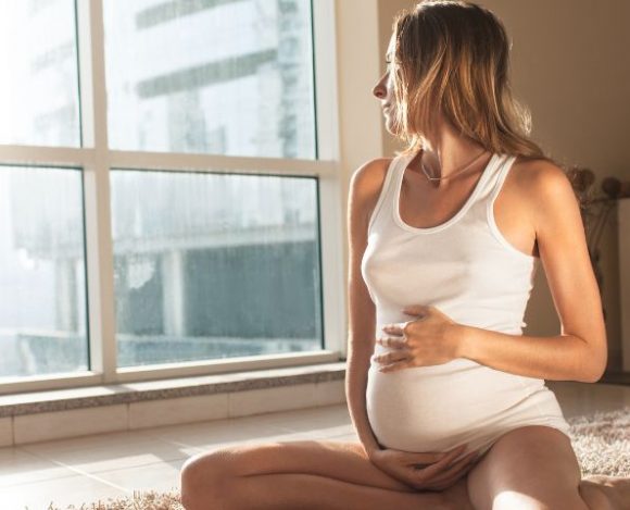 Kobieta w ciąży patrzy przez okno.