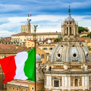 Ciekawostki o Włoszech – spadkobiercy Cesarstwa Rzymskiego. Na zdjęciu flaga Włoch, a w tle wspaniała rzymska architektura.