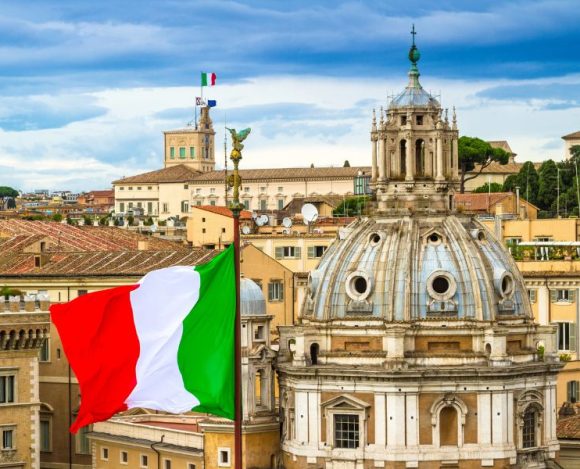 Ciekawostki o Włoszech – spadkobiercy Cesarstwa Rzymskiego. Na zdjęciu flaga Włoch, a w tle wspaniała rzymska architektura.