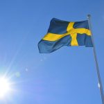 Szwecja – ciekawostki o kraju w środku Skandynawii. Na zdjęciu flaga Szwecji na tle słońca.