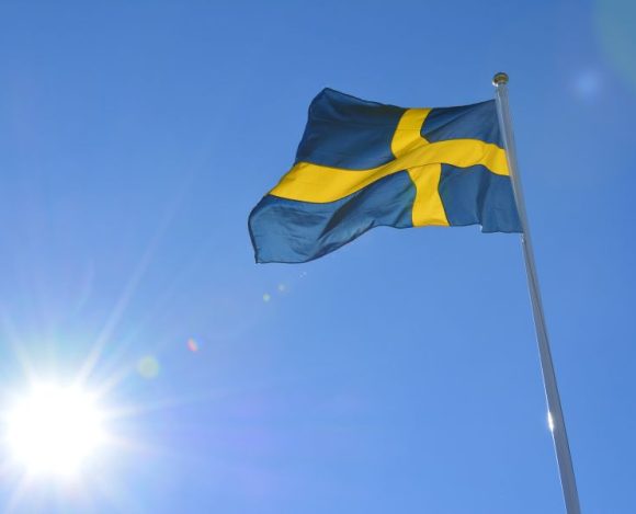 Szwecja – ciekawostki o kraju w środku Skandynawii. Na zdjęciu flaga Szwecji na tle słońca.
